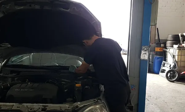 Mecànic de Juvany Motors treballant sota el capó d'un cotxe al taller, amb l'elevador blau al costat